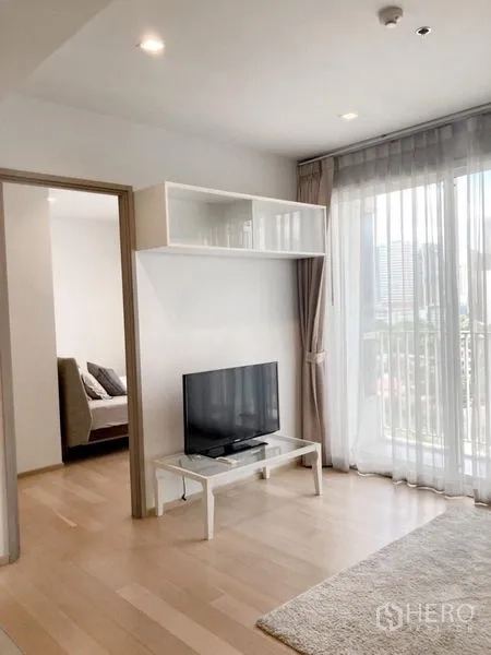 Condominium for rent in Watthana, Bangkok - TV wall with overhead storage, balcony-height glazing and doorway leading to the bedroom.