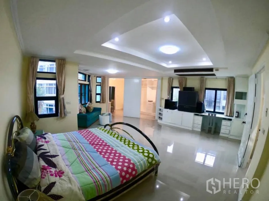 Townhouse for rent in Watthana, Bangkok - Large bedroom with seating nook, TV wall unit, ceiling lights and several windows.