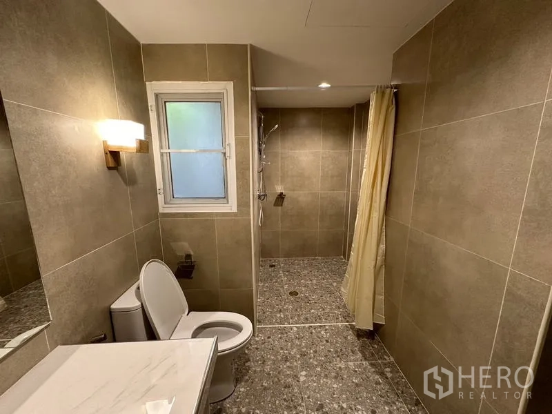 ทาวน์เฮาส์ ให้เช่าในPhra Khanong, Bangkok - ห้องน้ำปูกระเบื้องโทนอุ่น พร้อมโถสุขภัณฑ์ หน้าต่าง และโซนอาบน้ำแบบวอล์กอิน