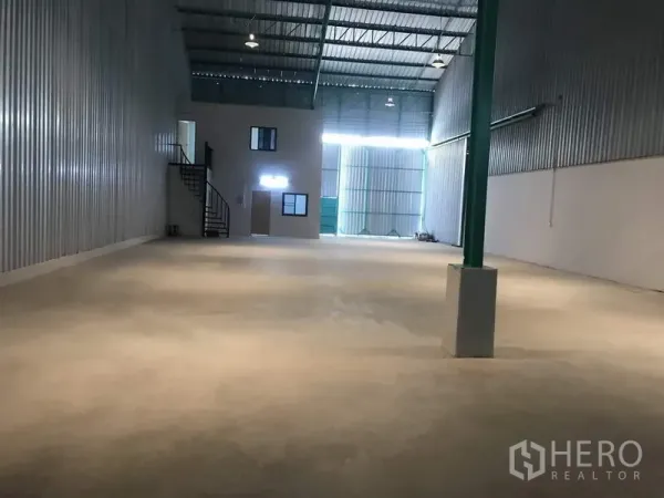 Factory for rent in Khlong Luang, Pathum Thani - Spacious high-ceiling warehouse interior with steel roof, metal cladding, concrete floor, mezzanine office and staircase, plus a wide drive-in entry.