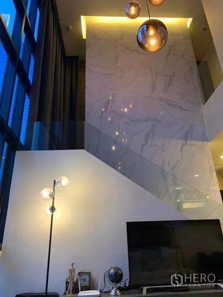Condominium for rent or sale in Huai Khwang, Bangkok - Marble-clad staircase wall with warm pendant lighting in a duplex condo.