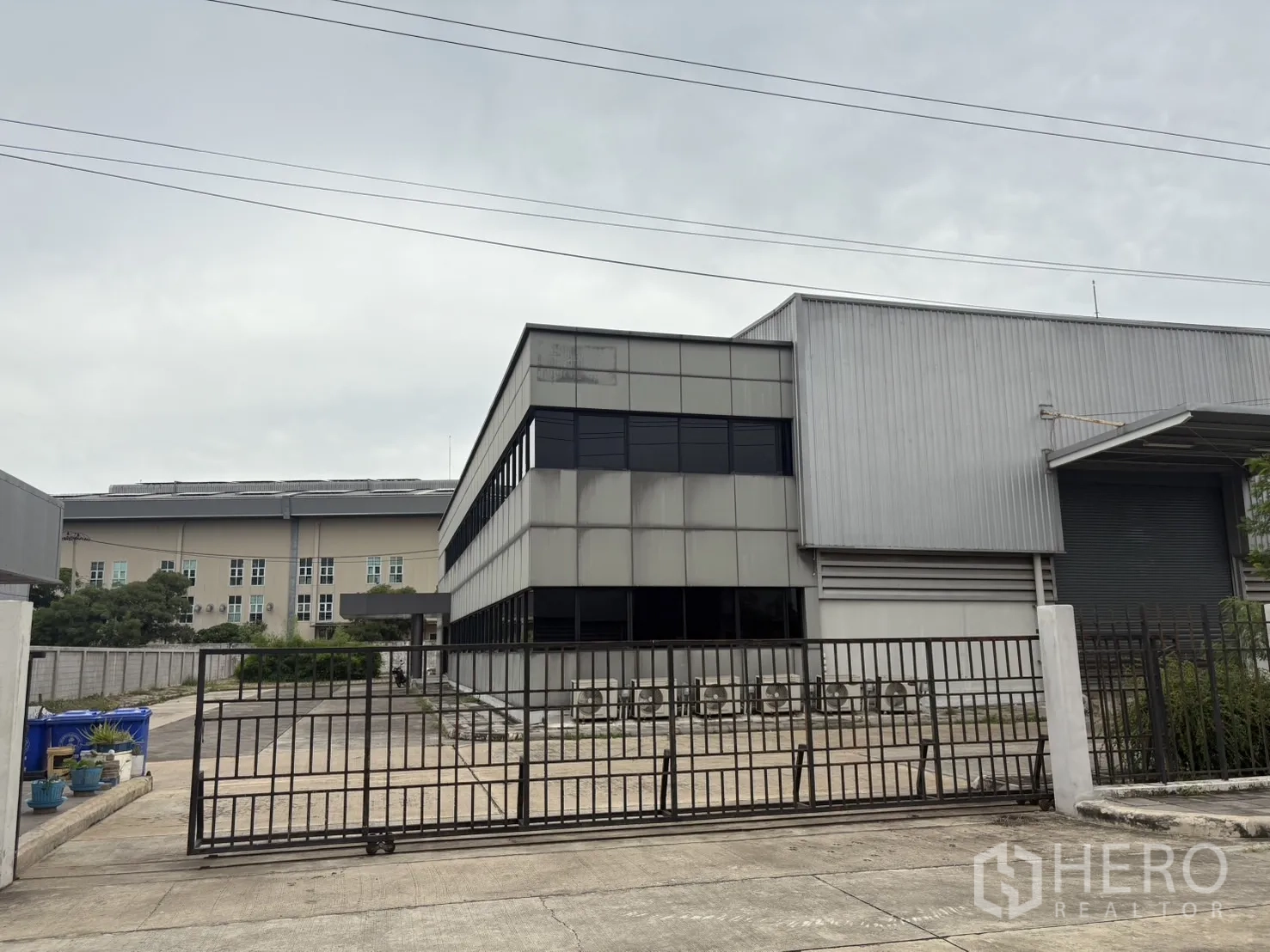 Factory for rent or sale in Samut Prakan - Gated entrance with metal fence facing the office and warehouse facade.