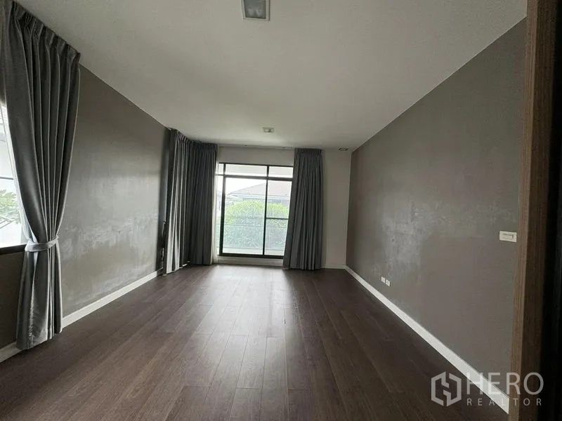 Detached House for rent in Samut Prakan - Spacious bedroom with large window, grey accent walls and curtains.