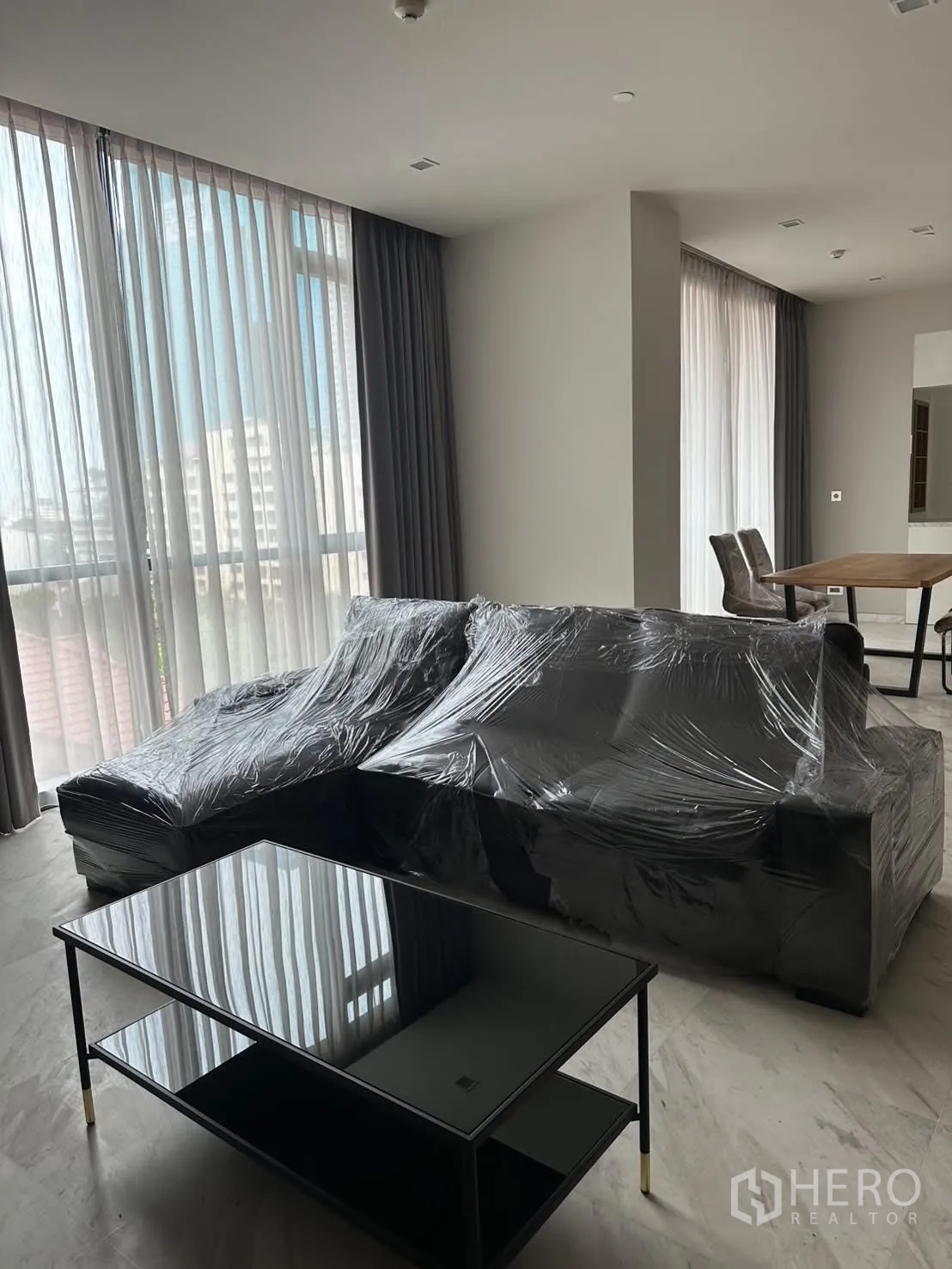 Condominium for rent or sale in Watthana, Bangkok - Open-plan lounge with sectional sofa and sheer curtains.