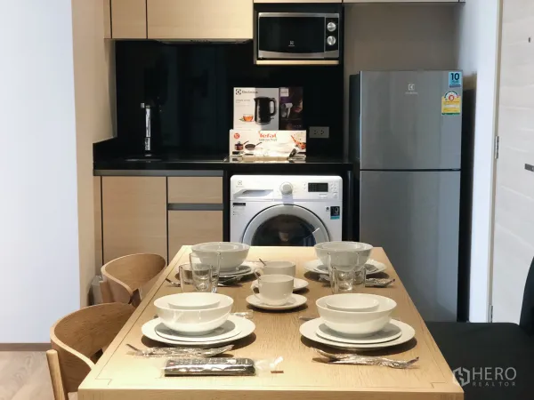 Condominium for rent in Khlong Toei, Bangkok - Modern kitchenette with dining table set, microwave, refrigerator and front-load washing machine.