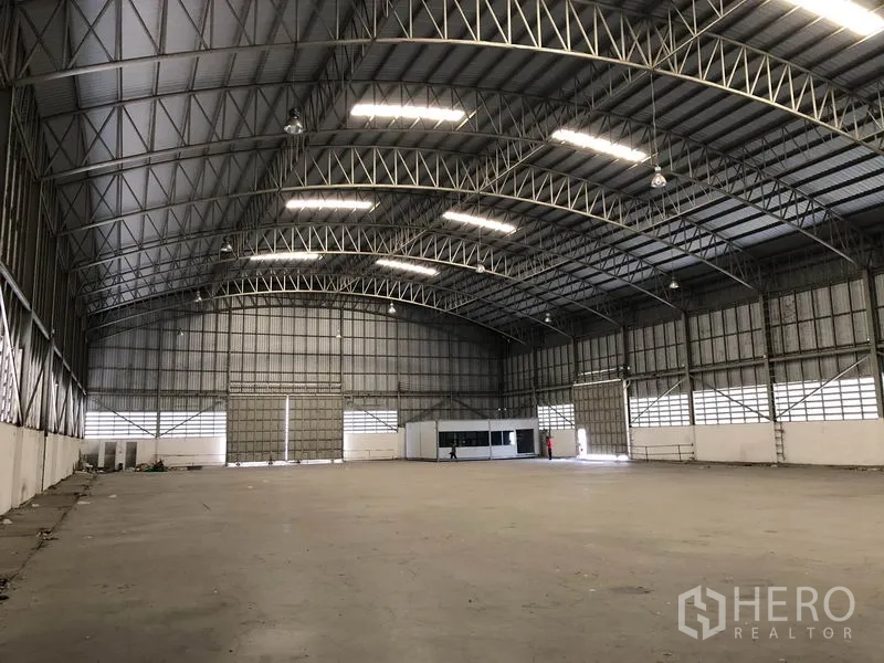 Warehouse for rent in Pathum Thani - Wide storage space showing a high ceiling, metal cladding walls and a corner office module.