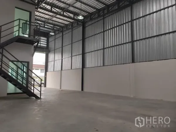 Warehouse for rent or sale in Lam Luk Ka, Pathum Thani - Open warehouse floor with ribbed metal walls, black steel columns and skylights for natural light.
