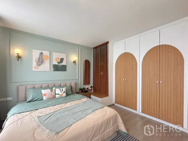 联排别墅 出租在Prawet, Bangkok - 主卧，淡色床品、壁灯与拱形木纹衣柜。