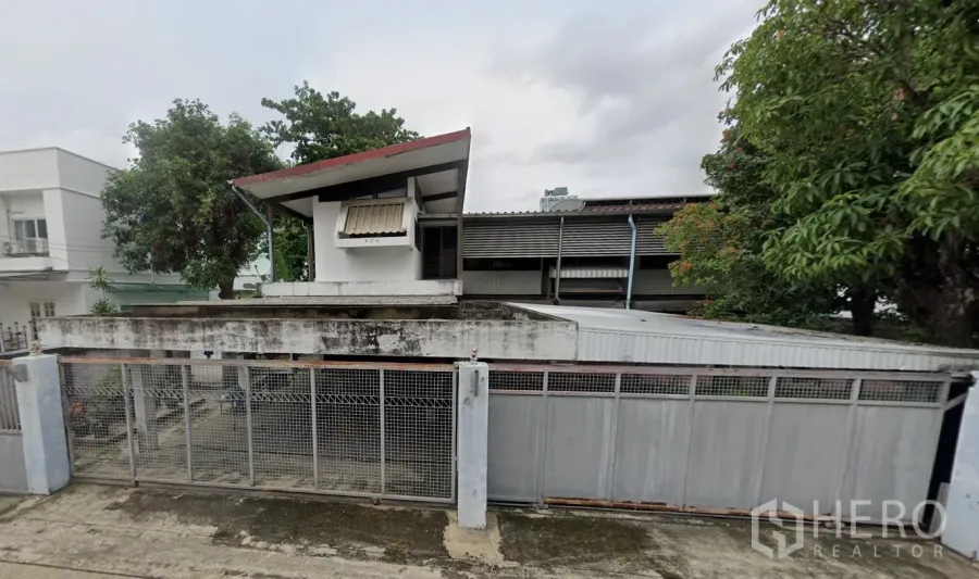 บ้าน ขายในKhlong Toei, Bangkok - มุมมองด้านหน้าบ้านเดี่ยวสองชั้น รั้วเหล็ก และต้นไม้ใหญ่