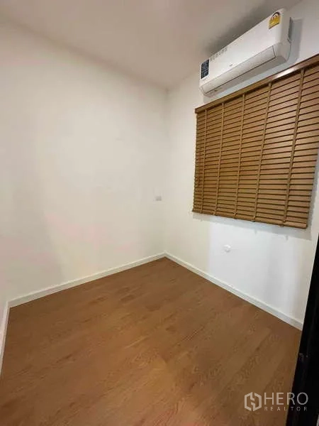 Townhouse for rent or sale in Bang Kapi, Bangkok - Compact air-conditioned room with window blinds and wood flooring.