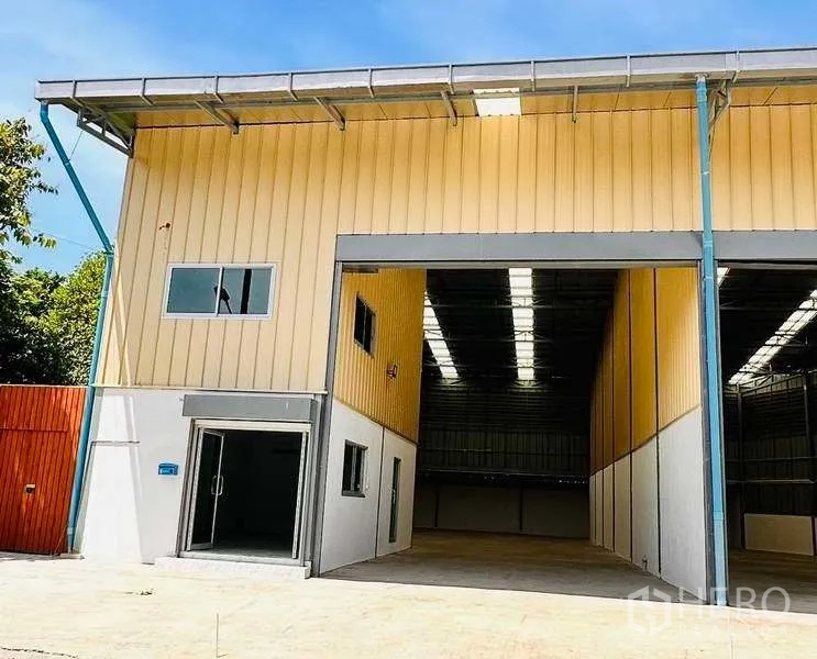 Warehouse for rent in Pak Kret, Nonthaburi - Modern yellow-clad warehouse exterior in Pak Kret, Nonthaburi with wide loading entrance and glass office door.