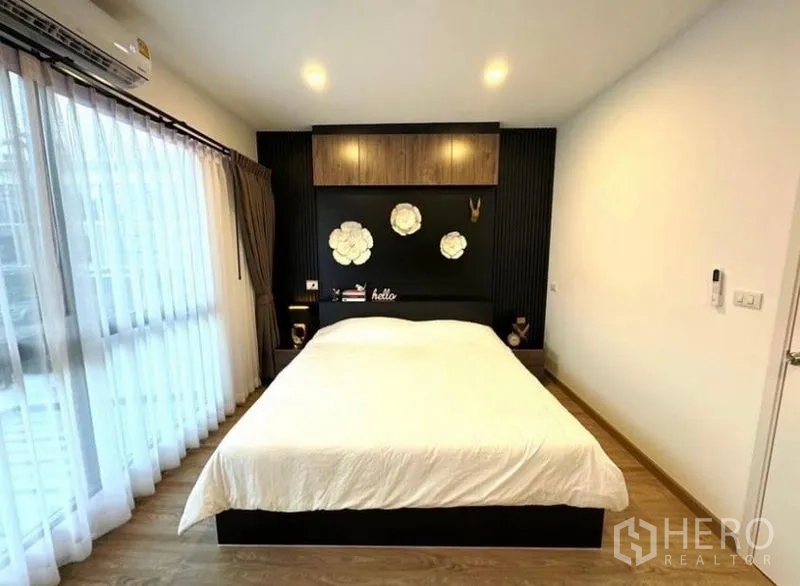 Townhouse for rent - Bright master bedroom with large window, sheer curtains, wood floors, and feature wall with overhead cabinet.