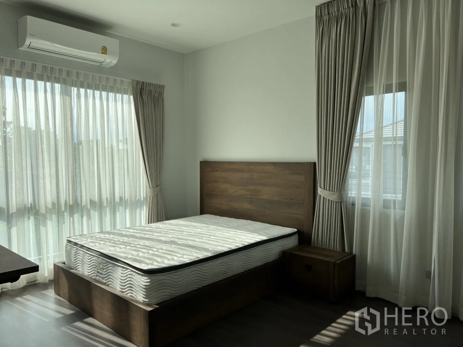 Detached House for rent in Bang Kapi, Bangkok - Sunlit guest bedroom with wooden bed, air conditioner, and layered curtains.