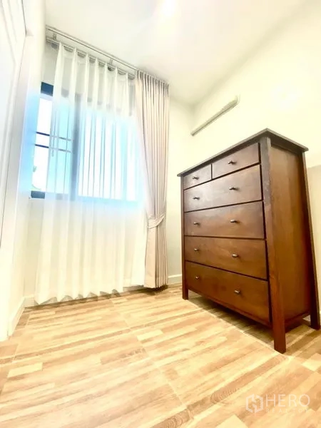 Townhouse for rent in Prawet, Bangkok - Compact dressing room with tall wooden chest and curtained window.