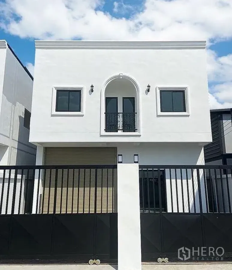 货栈 出租在Mueang Pathum Thani, Pathum Thani - 正面立面，黑色推拉大门与白色外墙，突出拱形阳台。