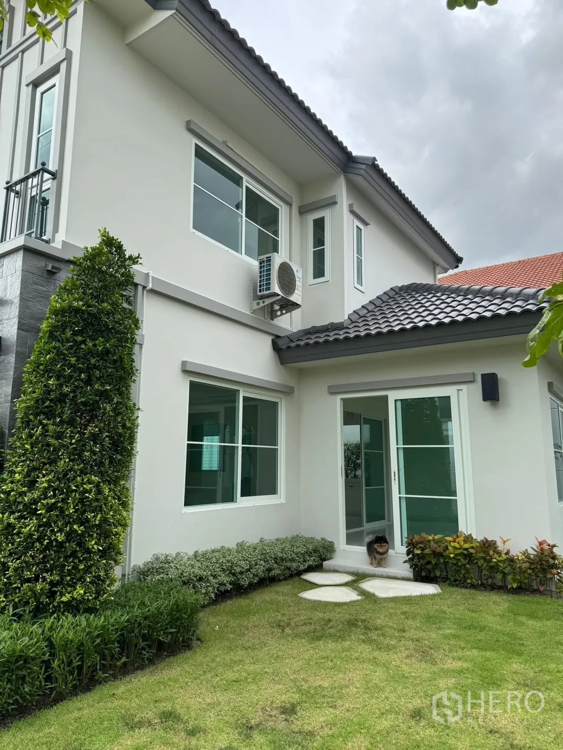 Detached House for rent in Bang Phli, Samut Prakan - Side view of the house opening to landscaped lawn with sliding glass doors and shrubs.