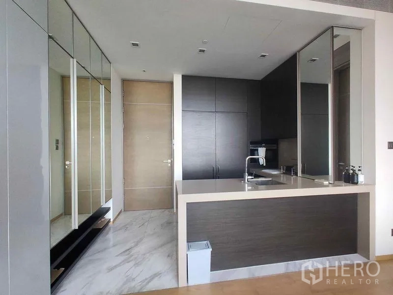 公寓 出租在Bang Rak, Bangkok - 入口走廊设镜面衣柜，对面为开放式中岛厨房与收纳柜。