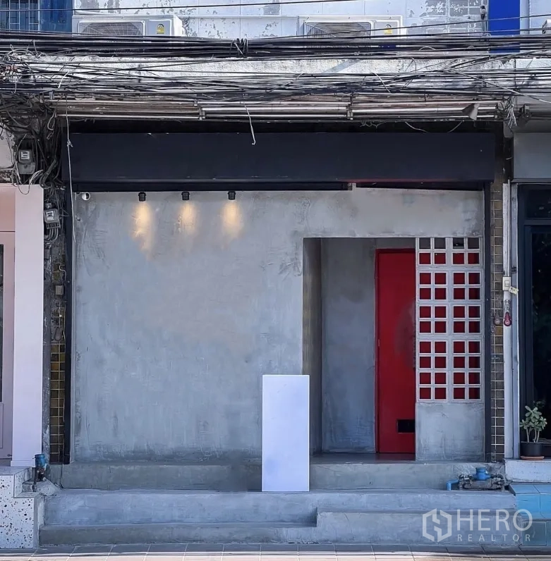 店屋 出租在Watthana, Bangkok - 极简混凝土店面立面，红色大门与射灯。