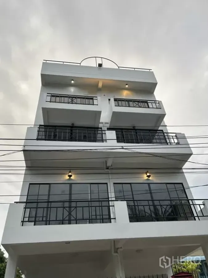 带办公室的家 出租或出售在Phra Khanong, Bangkok - 多层白色住宅办公楼外立面，带阳台和黑色框窗，黄昏景致。