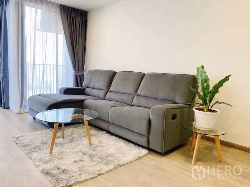 คอนโด ให้เช่า - ห้องนั่งเล่นติดระเบียง โซฟาเข้ามุม โต๊ะกระจกกลม และกระถางต้นไม้