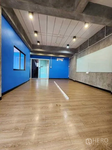 Office Space for rent or sale in Bueng Kum, Bangkok - Bright workspace with wood flooring, blue accent walls, ceiling spotlights and a glass door leading to a meeting room.
