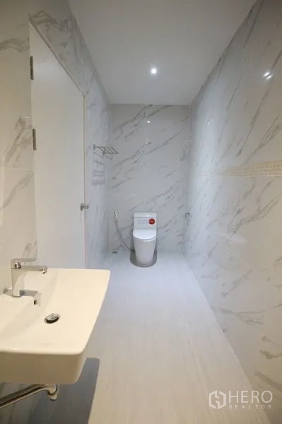 Detached House for rent in Chatuchak, Bangkok - Bathroom with marble‑effect wall tiles, white basin, modern toilet, and recessed ceiling light.