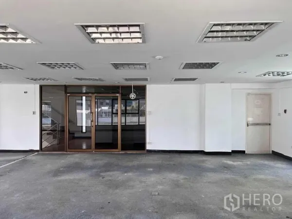 Shophouse for rent in Khlong San, Bangkok - Empty ground-floor space with glass entrance doors, white walls and fluorescent ceiling lights.