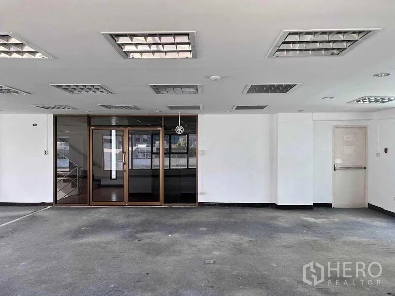 Shophouse for rent in Khlong San, Bangkok - Empty ground-floor space with glass entrance doors, white walls and fluorescent ceiling lights.