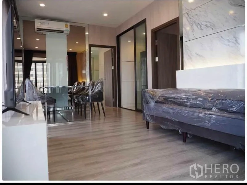 Condominium for rent in Huai Khwang, Bangkok - Bright living and dining area with wood floors, marble accent wall, glass partition and air conditioning in a Bangkok condo.