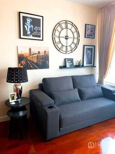 คอนโด ให้เช่าในKhlong Toei, Bangkok - ห้องนั่งเล่นโซฟาสีเทา นาฬิกาแขวนขนาดใหญ่ กรอบรูป และผ้าม่านแสงธรรมชาติ