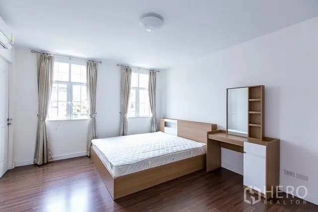 Townhouse for rent in Watthana, Bangkok - Second bedroom with light wood bed, dressing table, wood floors and two large windows.