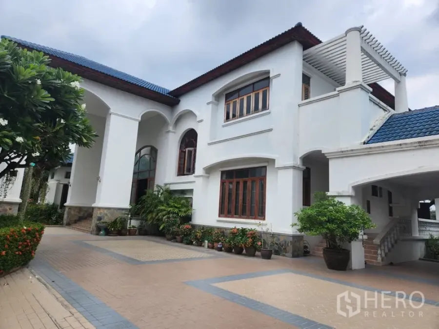 独立式住宅 出租在Prawet, Bangkok - 别墅侧立面，白墙蓝顶，连廊及盆栽绿植点缀。