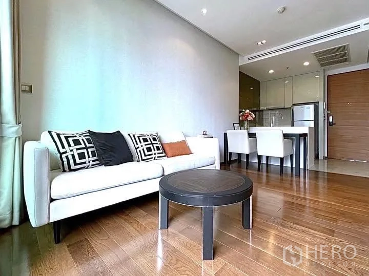 Condominium for rent in Khlong Toei, Bangkok - Lounge with white sofa, round coffee table, dining set, and compact kitchen.