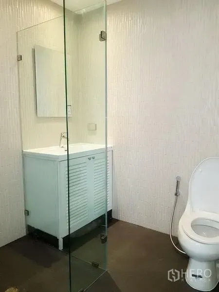 公寓 出租在Watthana, Bangkok - 极简卫浴，玻璃淋浴隔断与白色洗手台，墙面带纹理。