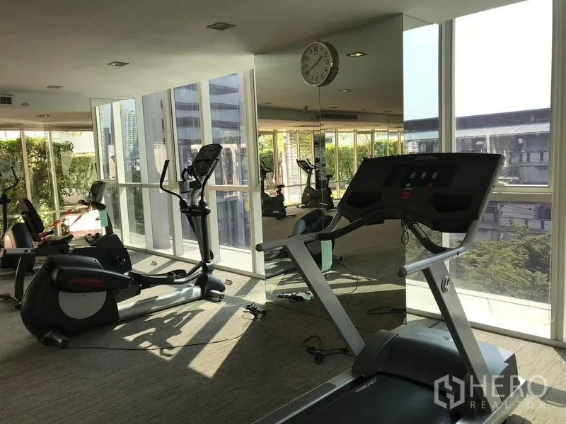 Condominium for rent or sale - Gym with treadmills and stationary bikes next to mirrored wall and large windows.