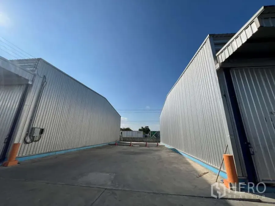 Warehouse for rent in Lat Krabang, Bangkok - Driveway between two metal warehouses with concrete yard and traffic cones.