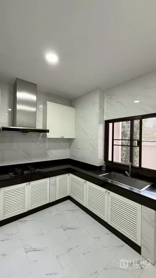 Detached House for sale in Saphan Sung, Bangkok - Bright L-shaped kitchen with white cabinets, black stone countertops, gas hob and stainless-steel hood.