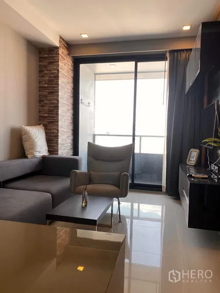 Condominium for rent in Bang Rak, Bangkok - Living room with sofa, armchair, TV wall unit, and sliding glass door to the balcony.