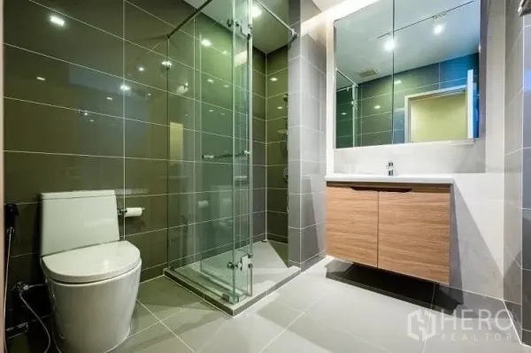 公寓 出售 - 现代卫浴，玻璃淋浴间、超大镜面与灰色瓷砖。