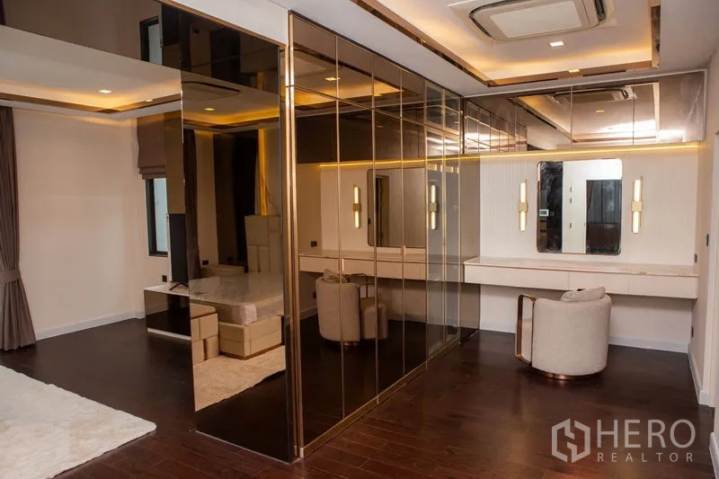 独立式住宅 出租或出售在Bangkok - 主卧配金色镜面衣柜、梳妆台与氛围照明。