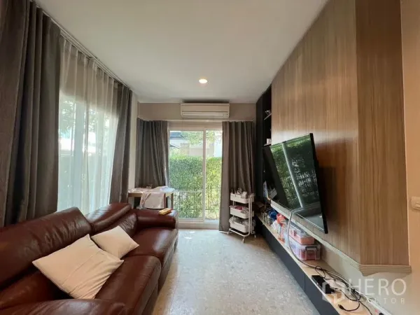 บ้าน ให้เช่าหรือขายในSaphan Sung, Bangkok - ห้องนั่งเล่นอบอุ่น โซฟาหนังสีน้ำตาล ผนังทีวี ประตูกระจกบานเลื่อน