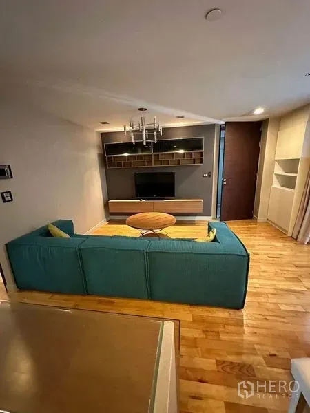 Condominium for sale in Bang Rak, Bangkok - Quad Silom condo living room with teal sofa, chandelier and TV wall unit.