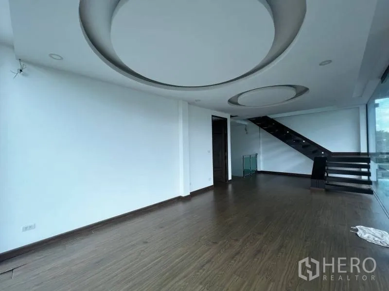 บ้าน ขายในLat Phrao, Bangkok - ห้องนั่งเล่นชั้นบนกว้าง พื้นไม้ ฝ้าเพดานลวดลายวงกลม และบันไดข้างผนังกระจก