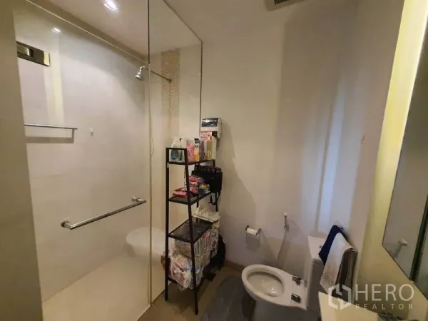 Condominium for rent in Yan Nawa, Bangkok - Modern bathroom with glass-enclosed shower, toilet and storage rack.