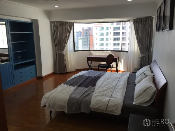 Condominium for sale in Watthana, Bangkok - Primary bedroom with bay window city view, blue built-in shelving, wood flooring and a desk by the window.