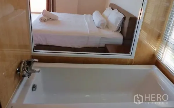 Condominium for sale in Bang Lamung, Chon Buri - Bathroom with white bathtub and a glass window connecting to the bedroom.