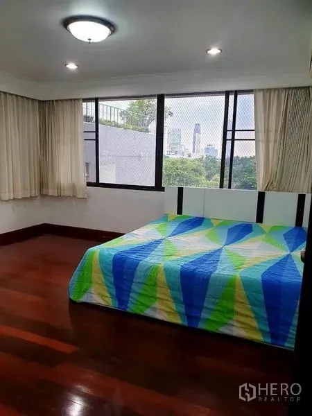 公寓 出租或出售在Watthana, Bangkok - 转角卧室，大窗户、城市景观与彩色床品的双人床。