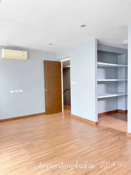 Townhouse for rent or sale in Don Mueang, Bangkok - Spacious bedroom with wooden flooring, built-in shelving and an open doorway.