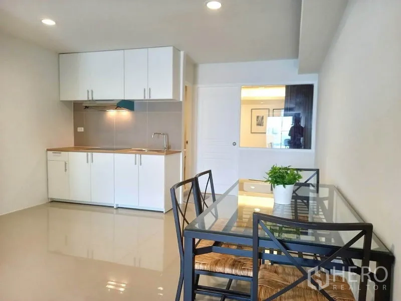 公寓 出租在Khlong Toei, Bangkok - 玻璃台面餐桌，旁为带吊柜的白色小厨房。