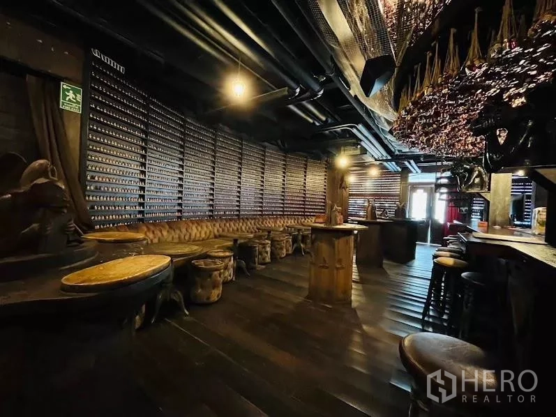 零售空间 出租在Watthana, Bangkok - 宽敞休闲区，长条纽扣沙发、高桌、深色木地板与外露天花。